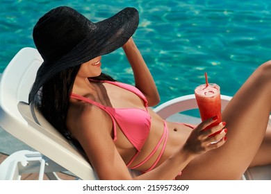 Side view of girl in hat and pink swimsuit lying on sunbed. Pretty young brunette female sunbathing, holding cocktail, smiling, enjoying leisure. Concept of summer and vacation. - Powered by Shutterstock