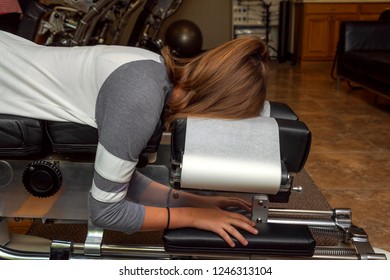Side view of a girl laying on a tilted chiropractic table with her head face down.   There is an exercise ball in the background and she has a ponytail holder on her wrist.