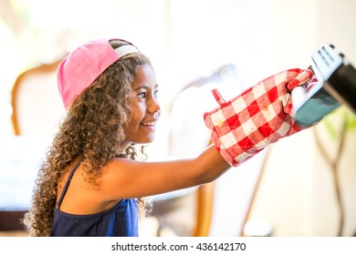 Side View Of Girl Wearing Oven Gloves Opening Oven Door Smiling