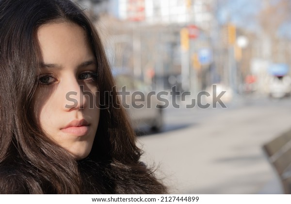 Side view of\
girl\'s face stands on a road. Blurry street with cars in the\
background. Details of girl\'s face. Sunlight hitting the face. Girl\
with grey eyes and dark brown\
hair.