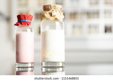 Side View Of Glass Bottles With A Homemade Raspberry Smoothie With Kefir Yogurt And Regular Kefir Yogurt With Paper Covers And Kitchen Shelf With Spices In The Background
