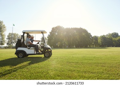 Side view of golfers riding golf cart on green lawn of golf field at warm sunny day. Concept of entertainment, recreation, leisure and hobby outdoors. Idea of frienship. Young caucasian male friends - Powered by Shutterstock