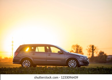 Side view of gray silver empty car parked in countryside on blurred rural landscape and bright orange clear sky at sunset copy space background. Transportation, traveling, vehicles design concept.
