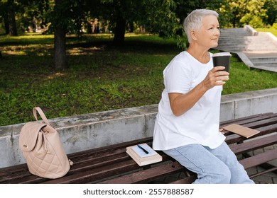 Side view of gray-haired 65s female enjoying free time in retirement sipping coffee sitting on bench at city park. Happy serene female resting alone enjoying summertime. Calm pensioner drinking tea. - Powered by Shutterstock