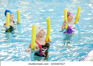 Side view at group of active senior women exercising in swimming pool, holding pool noodles and smiling, copy space - Powered by Shutterstock