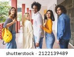 Side view of group of content multiethnic friends standing in street and looking at camera while enjoying stroll in summer