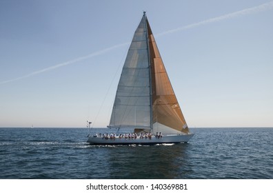 Side View Of A Group Of Crew Members Sitting On The Side Of A Sailboat In The Ocean Against Sky