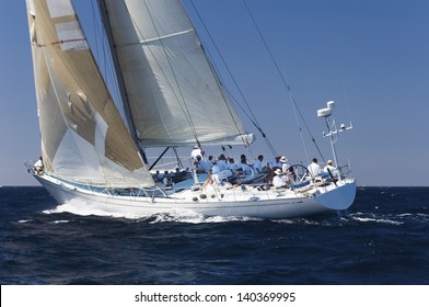 Side view of a group of crew members sitting on the side of a sailboat in the ocean against sky