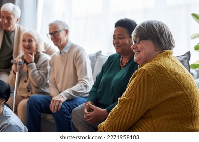 Side view at group of smiling senior people watching TV while sitting in row in retirement home facility - Powered by Shutterstock