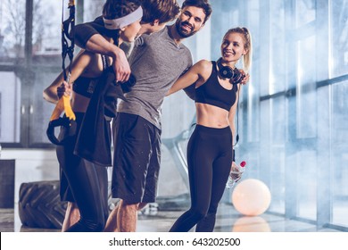 Side View Of Group Of Sportive People Near Trx Equipment In Gym