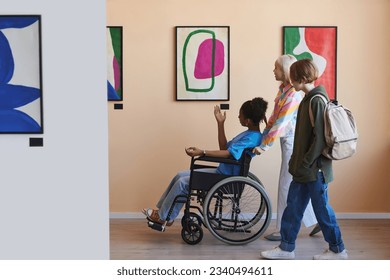 Side view of group of teenagers assisting friend with disability while visiting modern art gallery or museum - Powered by Shutterstock