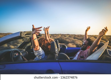 Side View Group Three Euphoric Friends In Convertible Car Twisting And Waving Two Curly Girls And Charming Bearded Man On Vacation Having Fun In Topless Auto Arms Up Palms Open Driving In The Sunlight