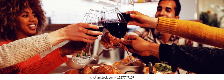 Side View Of A Group Of Young Adult Multi-ethnic Male And Female Friends Sitting At A Table At Home Set For Thanksgiving Dinner Making A Toast With Glasses Of Red Wine