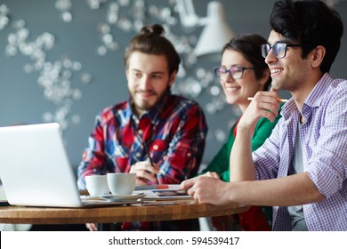 Side View Of Group Of Young Creative People Wearing Casual Clothes Collaborating At Meeting In Office And Smiling Looking At Laptop Screen