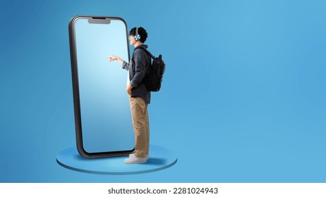 Side View Of Guy Using Large Cellphone Touching Screen Wearing Headphones Standing With Backpack Over Blue Studio Background. Panorama With Free Space For Text, Full Length - Shutterstock ID 2281024943