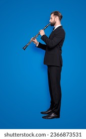 Side view half face, full size fullbody portrait of stylish talented musician with hairstyle in black tux with bow, pants, playing on bassoon, isolated on grey background