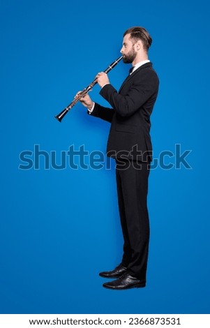 Side view half face, full size fullbody portrait of stylish talented musician with hairstyle in black tux with bow, pants, playing on bassoon, isolated on grey background