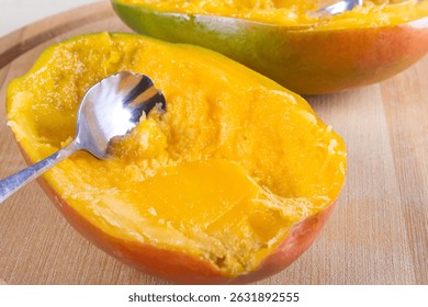 Side view of halve of mango and spoon on wooden background