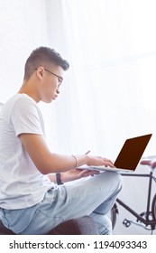 Side View Of Handsome Asian Man Using Laptop With Blank Screen On Sofa At Home