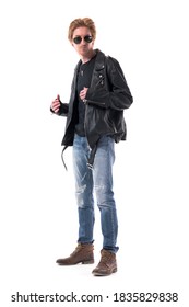 Side View Of Handsome Biker In Jeans And Black Leather Jacket Wearing Boots Getting Dressed. Full Body Isolated On White Background.