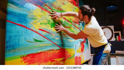 Side view of handsome Caucasian young talented creative male contemporary artist works in art studio emotionally drawing on large canvas with his hands, abstract artwork, painter concept - Powered by Shutterstock