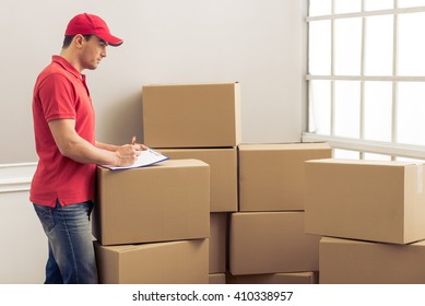 Side view of handsome delivery worker signing documents while standing among cardboard boxes