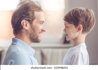 Side View Of Handsome Father And His Cute Son Looking At Each Other And Smiling While Spending Time Together At Home