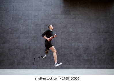 Side View Of Handsome Fit Caucasian Sportsman With Artificial Leg Running Outside.