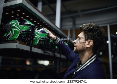 side view of handsome man choosing helmet for karting inside of karting locker room, motorsport