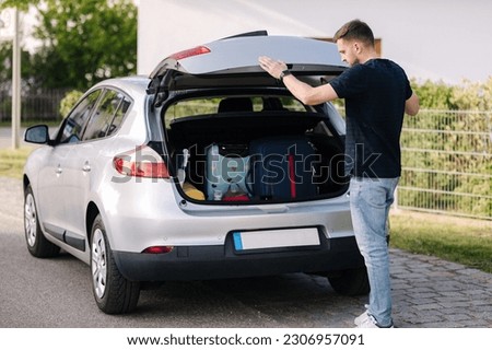Side view of handsome man close hatchback car for trunk. Vehicle and automotive travel road trip. Holliday on summer vacation concept