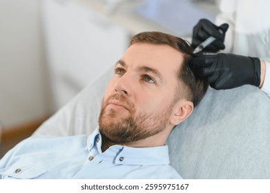 Side view of handsome man getting hair treatment at beauty salon. Man having mesotherapy session at aesthetic clinic, therapist hands in gloves making injection in scalp, closeup