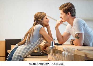 side view of handsome man and young woman flirting and smiling each other while working n cafe