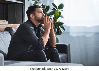 Side View Of Handsome And Pensive Man Sitting On Sofa And Looking Up In Apartment 