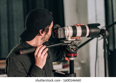 Side view of handsome videographer with camera on tripod in photo studio