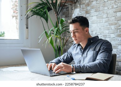 Side view handsome young businessman in eyewear working with computer remotely, sitting at wooden table in office. Pleasant happy man communicating in social network, searching information online. - Shutterstock ID 2258784237