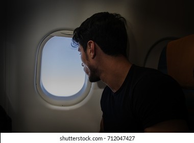 Side View Of Handsome Young Man Against Plane Window Sitting And Looking Out