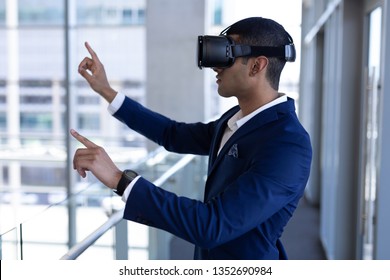 Side view of handsome young mixed-race businessman using virtual reality headset standing in modern office - Powered by Shutterstock