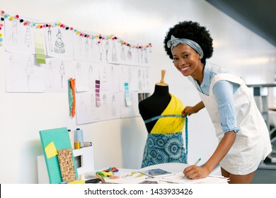 Side view of happy African american female graphic designer writing on paper while measuring mannequin in office - Powered by Shutterstock