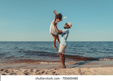 Side View Of Happy African American Father Playing With Cute Little Daughter On Beach