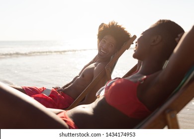 Side View Of Happy African-american Couple Interacting With Each Other While Relaxing In A Beach Chair On The Beach