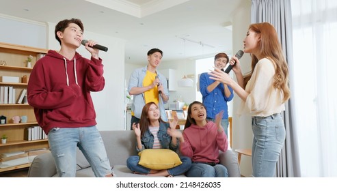 Side View Of Happy Asian Friends Singing Karaoke Clapping Together In The Room Man And Woman Duet With Microphone