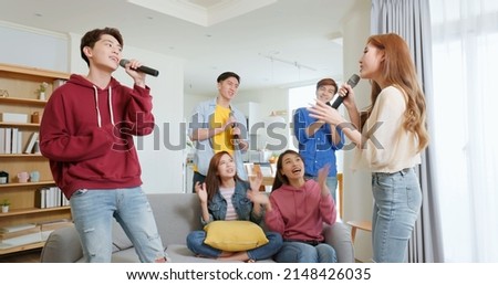 side view of happy asian friends singing karaoke clapping together in the room man and woman duet with microphone