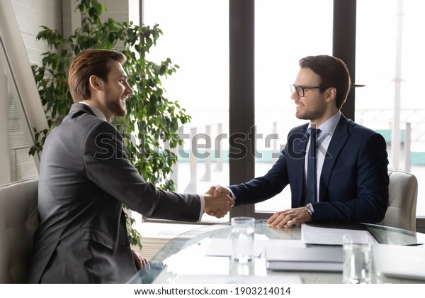 Side view happy business partners shaking\
hands, closing deal, making agreement, sitting at table in modern\
office, smiling hr manager congratulating successful candidate\
after interview, handshake