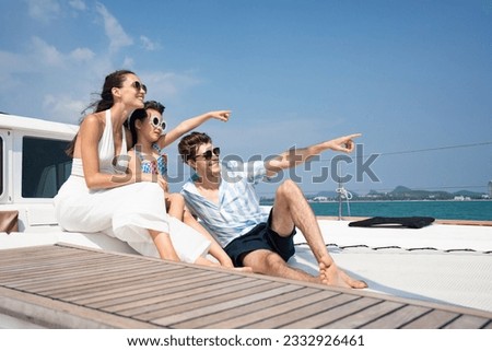 Side view of a happy Caucasian family with father, mother, and little daughter, wearing sunglasses, looking and point forward while relaxing sitting on a luxury yacht during a sailing trip on the sea.