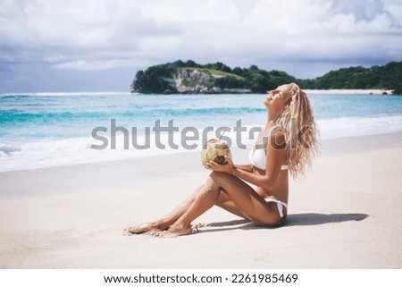 Side view of happy female tourist in swimwear lying on sandy beach and sunbathing while relaxing and enjoying coconut drink. Go Everywhere and enjoying freedom