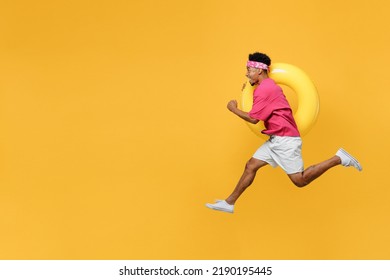 Side view happy fun cool young man he wear pink t-shirt near hotel pool jump high run fast hurrying up hold inflatable rubber ring isolated on plain yellow background. Summer vacation sea rest concept - Powered by Shutterstock