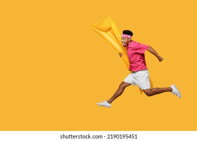 Side View Happy Fun Cool Young Man He Wear Pink T-shirt Near Hotel Pool Jump High Run Fast Hurrying Up Hold Inflatable Mattress Isolated On Plain Yellow Background. Summer Vacation Sea Rest Concept