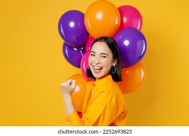 Side view happy fun excited exultant young woman wears casual clothes celebrating near balloons do winner gesture clench fist isolated on plain yellow background. Birthday 8 14 holiday party concept - Shutterstock ID 2252693823