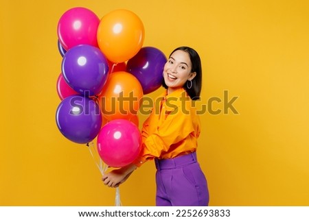 Side view happy fun smiling young woman wearing casual clothes celebrating holding bunch of colorful air balloons look camera isolated on plain yellow background. Birthday 8 14 holiday party concept