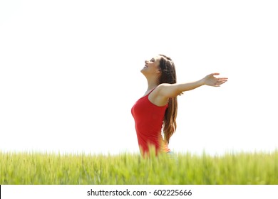 Side view of a happy girl wearing res shirt breathing fresh air and raising arms in a field with a white sky in the background